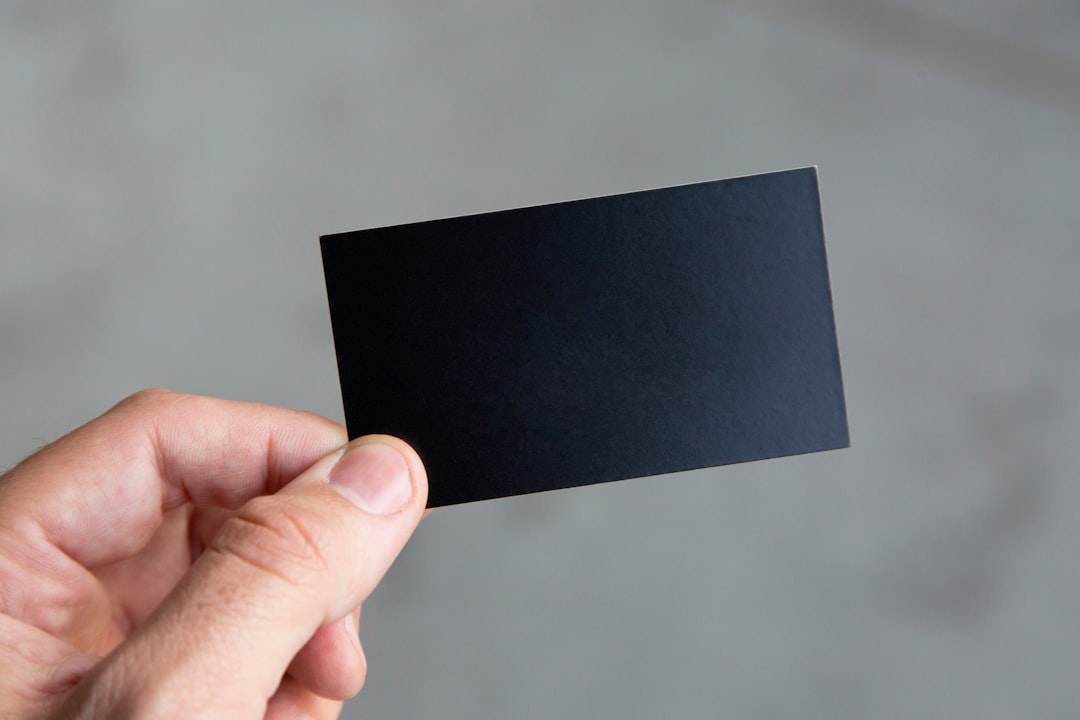Person holding a blank black business card in their hand against a blurred background.